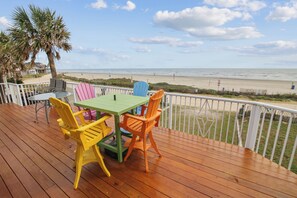 A wooden deck with a table and chairs, overlooking a beach.