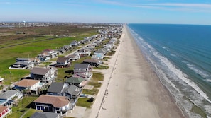 A coastal residential area with houses along the beach, a clear sky, and a distant bridge.