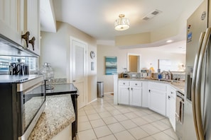A modern kitchen with white cabinets, a granite countertop, stainless steel appliances, and a ceiling light fixture. - Beachfront Seashell by Ryson Vacation Rentals (Galveston)