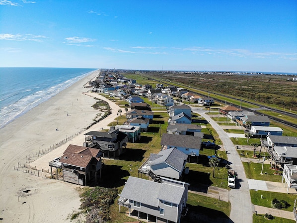 A coastal residential area with houses along the beach, a road, and a clear view of the ocean.