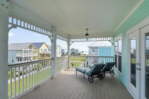A covered porch with a white railing, two lounge chairs, and a view of neighboring houses.