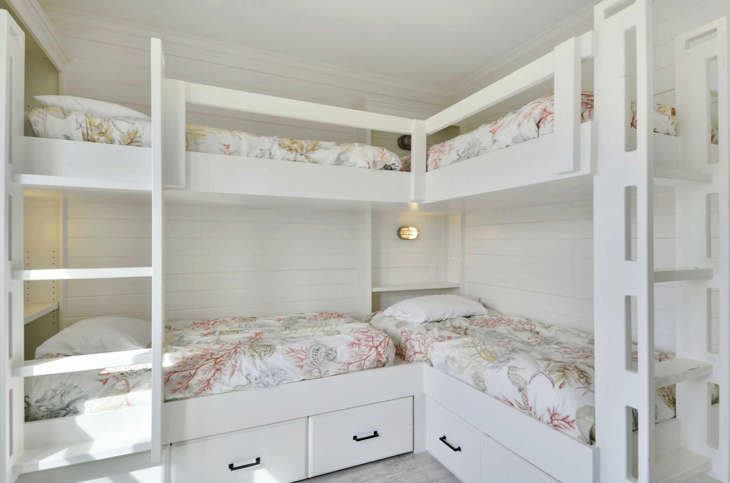 Habitación con literas dobles, cada una con ropa de cama floral, y una lámpara de pared.