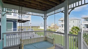 A covered porch with a wooden bench, white railings, and a view of other buildings.
