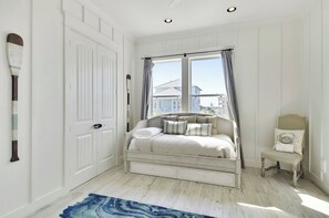 Un dormitorio con cama, una silla, una ventana con cortinas, una puerta y una tabla de surf fijada a la pared.