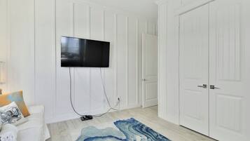 A room with a flat-screen TV mounted on the wall, a white door, and a blue marble-patterned rug on the floor.