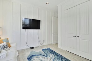 Una habitación con un televisor de pantalla plana montado en la pared, una puerta blanca y un tapete azul con diseño de mármol en el suelo.