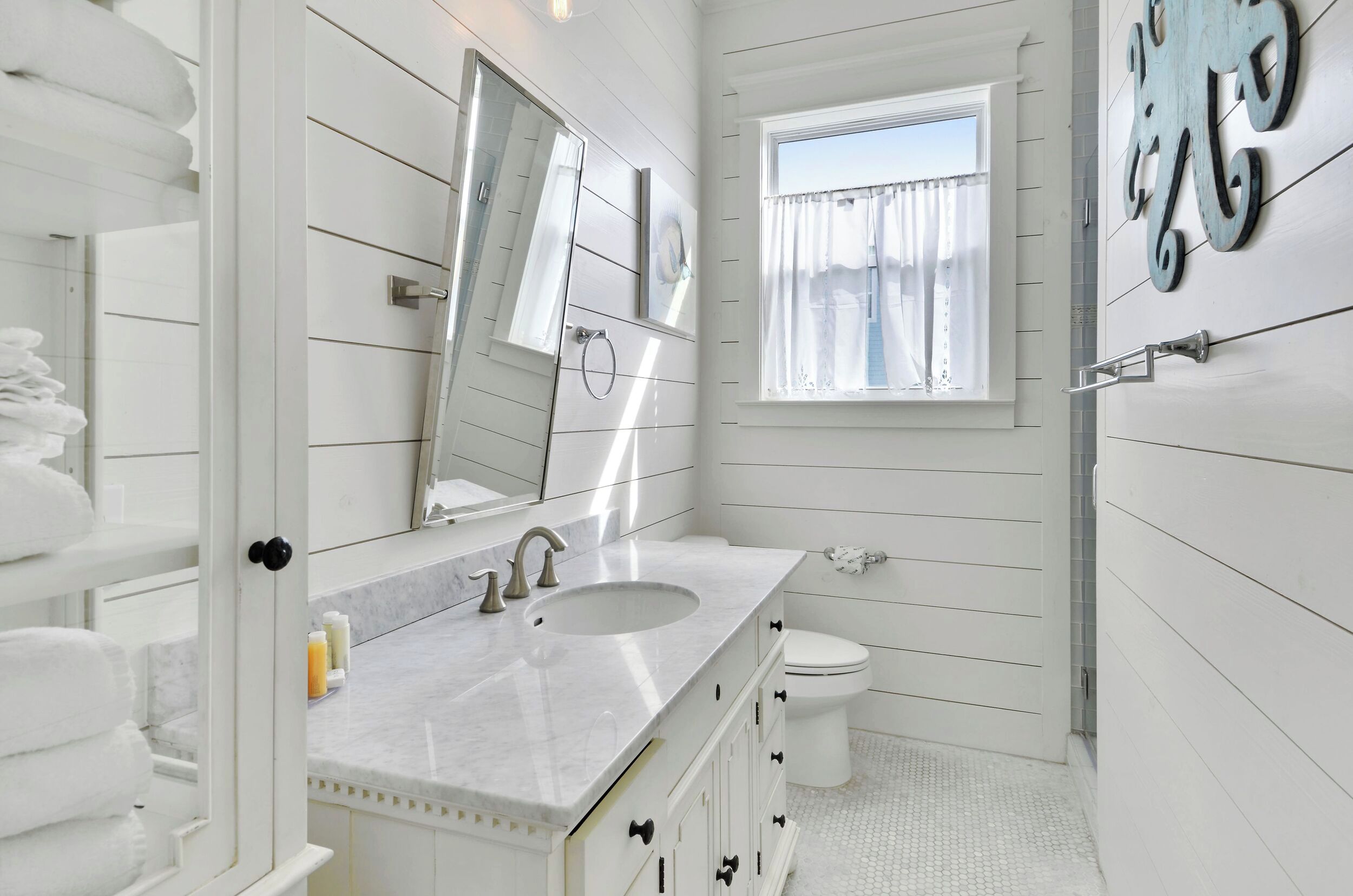 Ein Badezimmer mit weißem Waschtisch, Waschbecken, Toilette und einem Fenster mit Vorhängen.