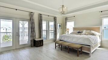 A bedroom with a large bed, a bench, a chest of drawers, and a view of the outside balcony.