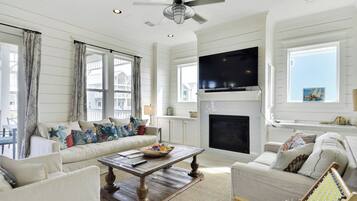 A spacious living room with a fireplace, a television mounted above it, and a large window with curtains.