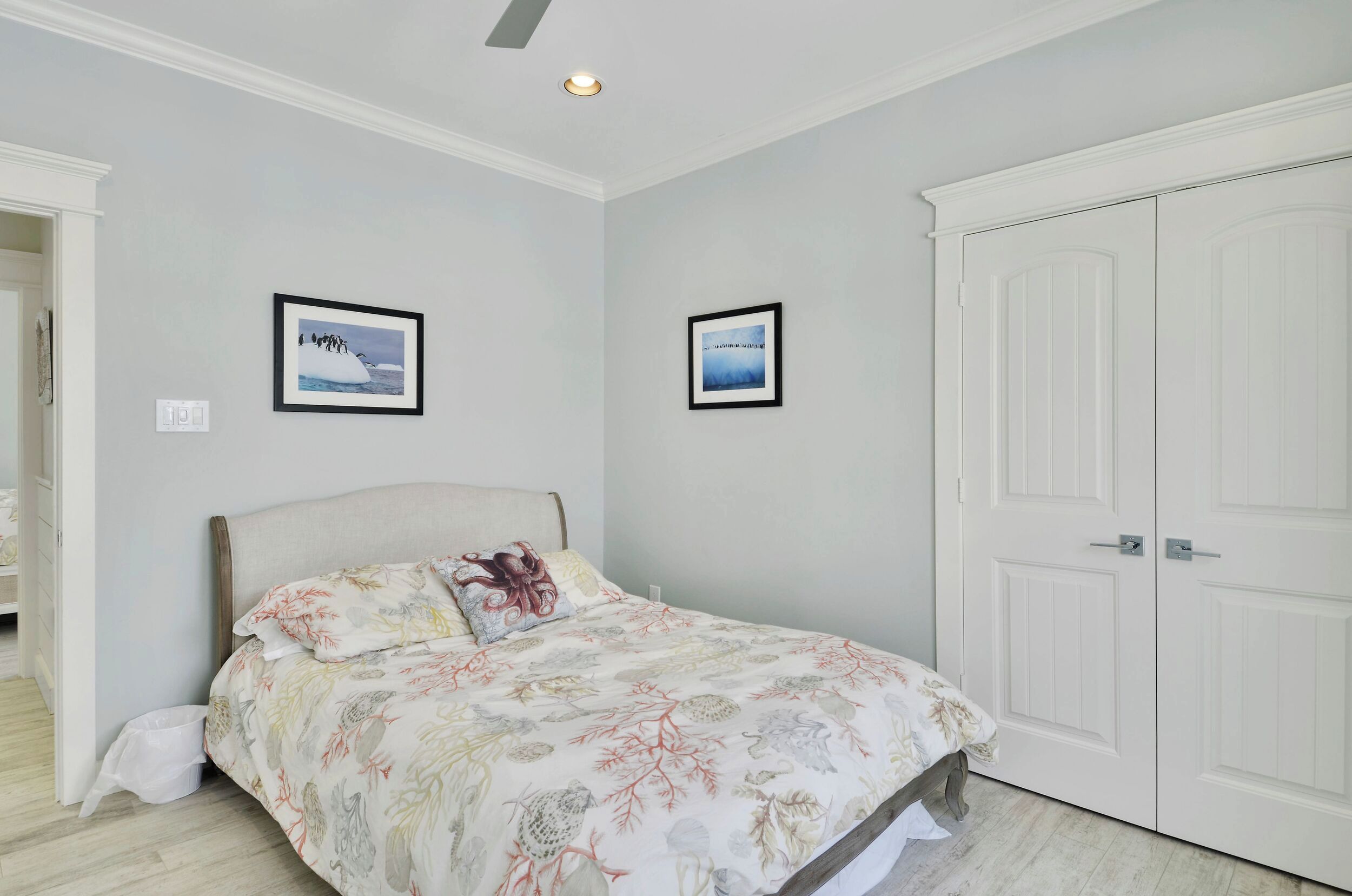 A bedroom with a bed, two framed pictures on the wall, and a white wardrobe.