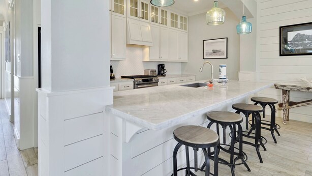 Una cocina moderna con armarios blancos, una isla grande con taburetes y luces colgantes.