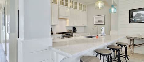 Una cocina moderna con armarios blancos, una isla grande con taburetes y luces colgantes.