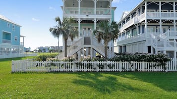 A coastal building with multiple balconies, a white picket fence, and lush greenery.