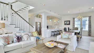 A spacious living room with a white staircase, a kitchen area, and a dining space with bar stools.