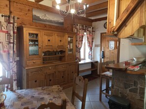A rustic kitchen with wooden cabinets, a stone countertop, and a dining area with a table and chairs.
