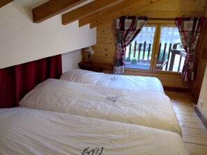 A cozy bedroom with two beds, wooden beams, a window with curtains, and a small table. - Henriette's Big Farm (Samoens)