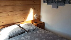 Makuuhuone, jossa on puinen katto, kuviollinen vuodevaatteilla varustettu sänky, yöpöytälamppu ja seinälle ripustettu taulu.