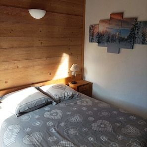 A bedroom with a wooden ceiling, a bed with patterned bedding, a bedside lamp, and a wall-mounted picture.