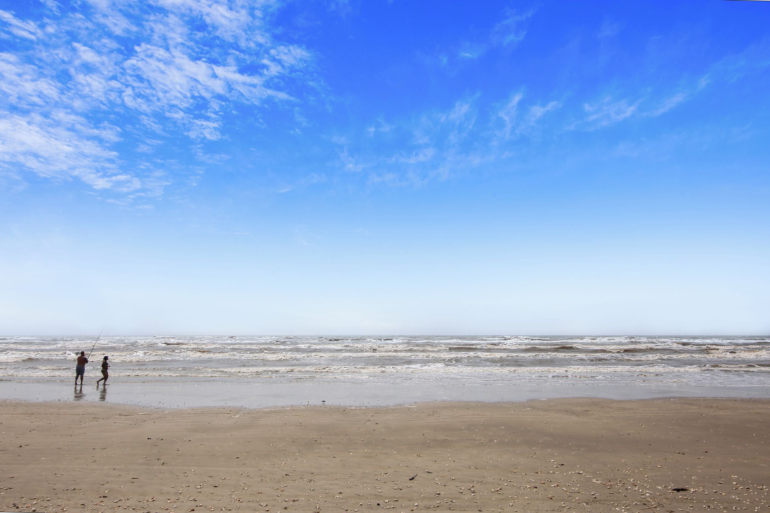 A beach with two people walking along the shore.