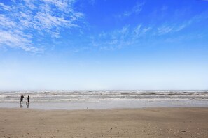 A beach with two people walking along the shore. - Bermuda Beachfront by Ryson Vacation Rentals (Galveston)