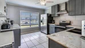 Une cuisine moderne avec des meubles gris, un réfrigérateur en acier inoxydable, un four encastré et une fenêtre avec des stores.