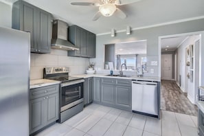 A modern kitchen with grey cabinets, stainless steel appliances, and a tiled floor.