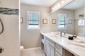 A bathroom with a large mirror, two sinks, a toilet, and a shower area.