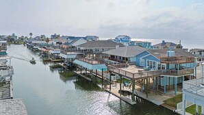 A waterfront property with multiple docked boats, a pier, and a series of connected buildings with balconies. - 1 Mi to Sea Isle Beach: Canal-Front Gem w/ Dock! (Galveston)