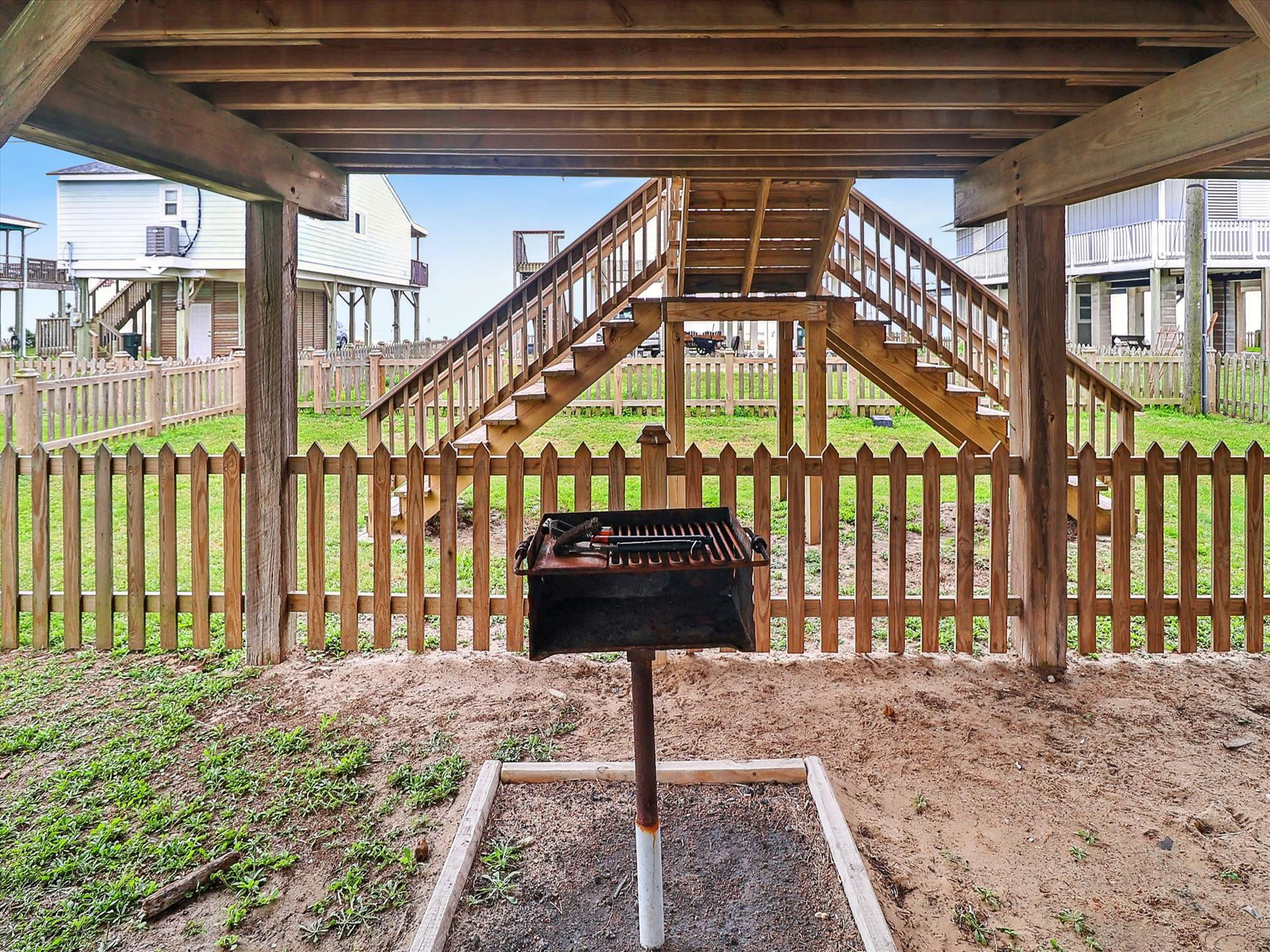 Een barbecue onder een houten pergola, met een houten omheining en een trap naar een balkon.