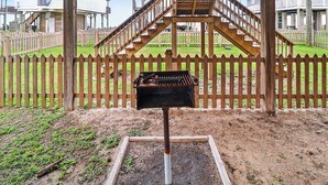 Una barbacoa sota una pérgola de fusta, amb una tanca de fusta i unes escales que condueixen a un balcó.
