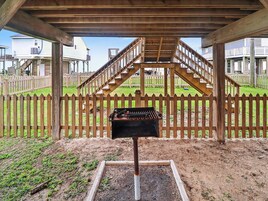 Un barbecue installé sous une pergola en bois, avec une clôture en bois et un escalier menant à un balcon.