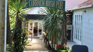 Ein Weg führt zu einem Gebäude, an dem ein Schild mit der Aufschrift 'The Currrach Irish Pub' zu sehen ist.