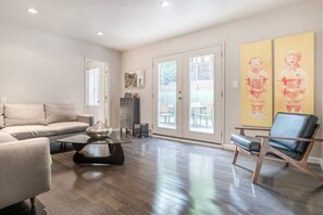 Relax in this stylish living room with a sofa, armchair, and coffee table, surrounded by artwork and leading out to an outdoor area.