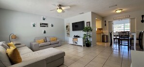 A living room with a grey sofa, a TV, and a dining area with a table and chairs.