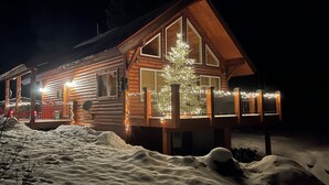 Una cabaña de troncos con un porche cubierto de nieve y un árbol de Navidad iluminado.