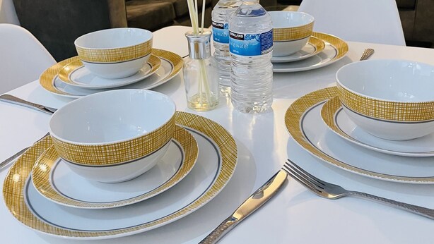 A dining table set with white plates and gold accents, surrounded by modern furniture and a large window. - Modern city centre two bedroom fully equipped apartment (Derby)