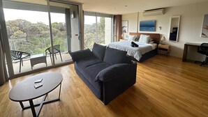 A modern hotel room with a large bed, a sofa, a dining table, and a balcony with chairs. - Torquay285 King Studio Beachfront Resort (Torquay)