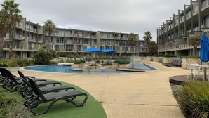 A pool area with lounge chairs and umbrellas, surrounded by a multi-story building with balconies. - Torquay285 King Studio Beachfront Resort (Torquay)