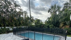 Ein Poolbereich mit rundem Tisch und vier Stühlen, umgeben von einem Zaun und üppiger Bepflanzung.