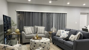 Ein modernes Wohnzimmer mit einem grauen Sofa, einem gemusterten Ottomanen und einem gestreiften Vorhang im Hintergrund.