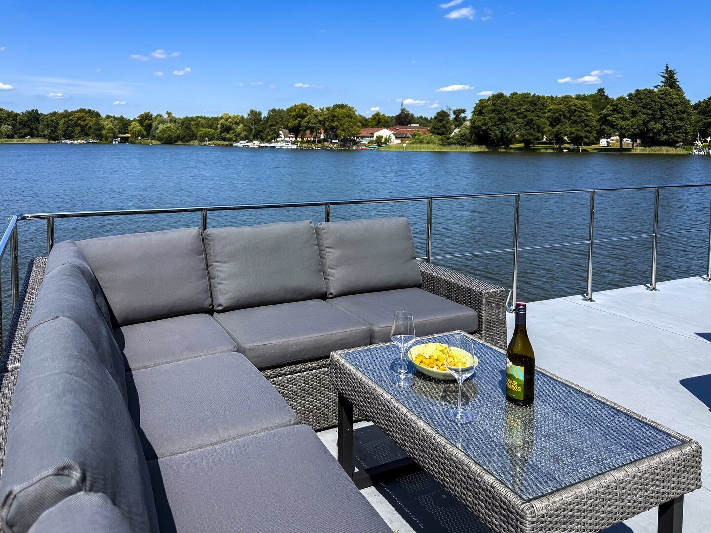 Eine Terrasse mit einer grauen Couch und einem Glastisch, einer Weinflasche und einer Obstschale.