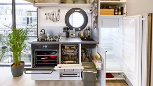 A compact kitchen with built-in appliances, a window, and a potted plant. - Houseboat Suite GRAND PLAISIR – Luxury houseboat, no license required (Zehdenick)