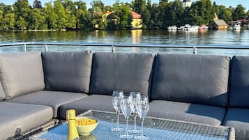 A boat deck with a cushioned seating area, a table with a bottle of champagne, glasses, and a bowl of snacks.
