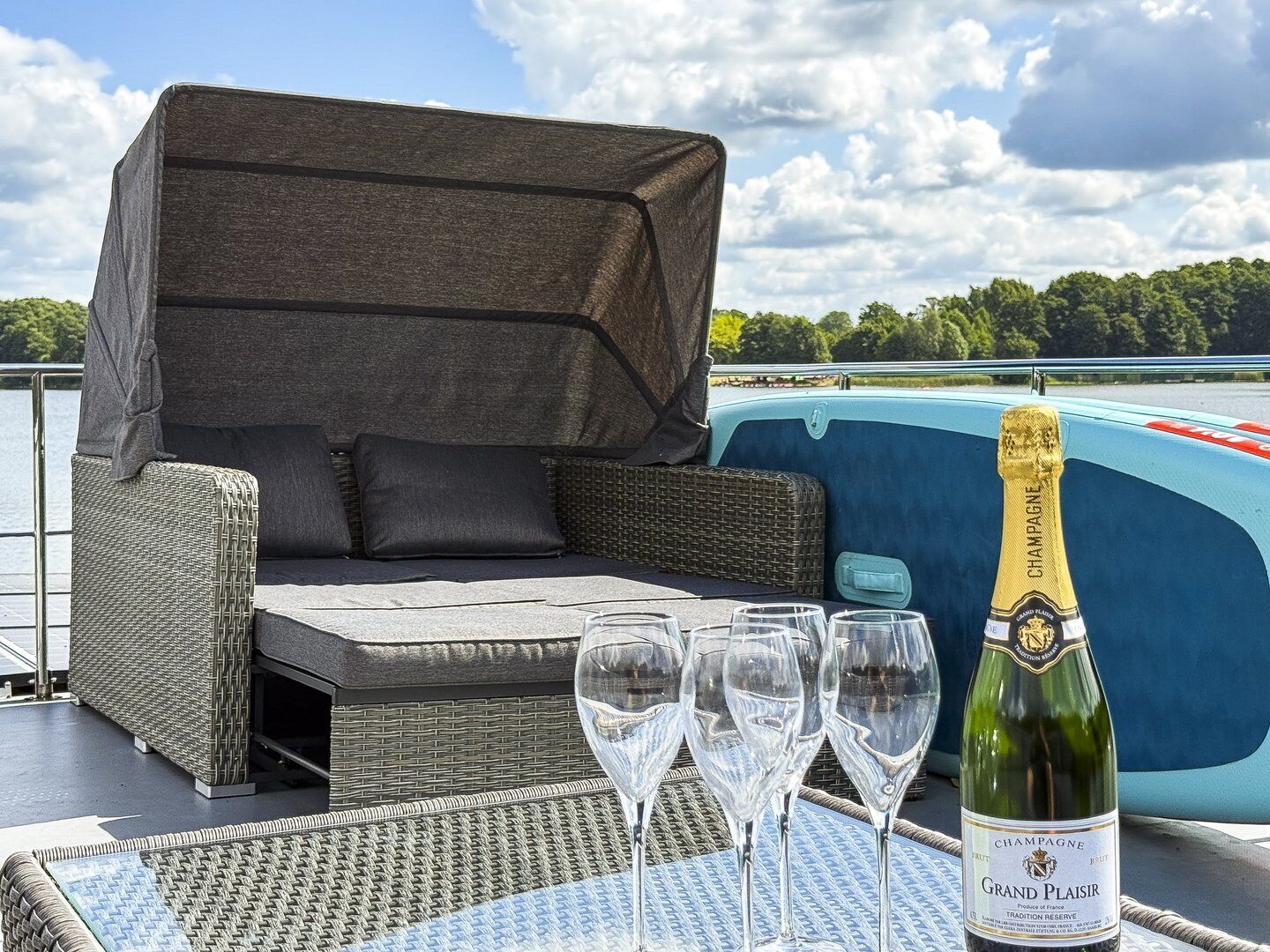 Ein Sitzbereich im Freien aus Weidwerk mit einer überdachten Couch, einem Tisch mit vier Weingläsern und einer Champagnerflasche auf einem Boot.