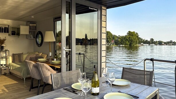 A dining area with a table set for two, overlooking a body of water. - Houseboat Suite GRAND PLAISIR – Luxury houseboat, no license required (Zehdenick)