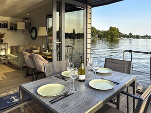 Un coin repas avec une table dressée pour deux personnes, donnant sur un plan d’eau.
