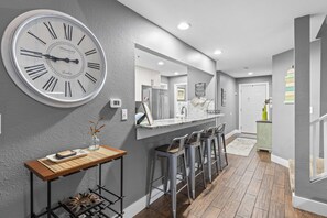 Una cocina moderna con un gran reloj de pared, taburetes de bar y una mesa de madera.