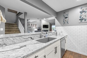 A kitchen with a granite countertop, stainless steel sink, and white cabinetry.