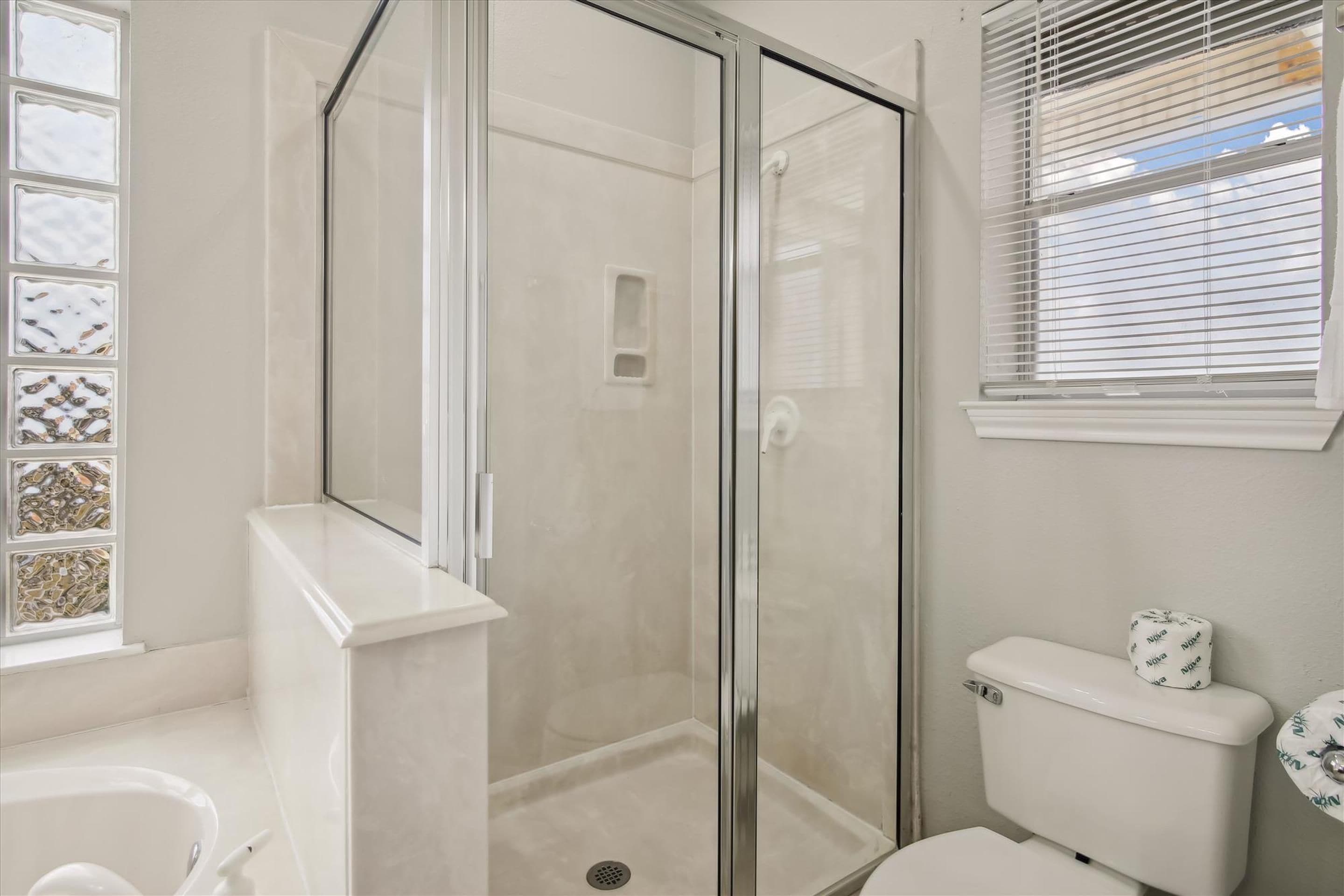 A bathroom with a glass-enclosed shower, a toilet, and a sink.