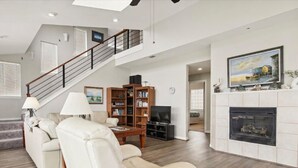A spacious living room with a fireplace, a staircase, and a large painting on the wall. - Brannen's Beachfront by Ryson Vacation Rentals (Galveston)